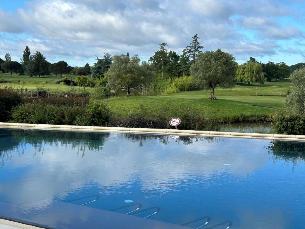 a swimming pool with a golf course in the background at Mercure Toulouse Aéroport Golf de Seilh in Seilh