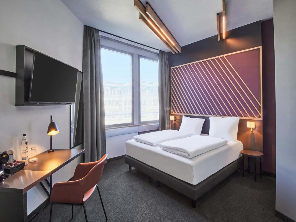 a hotel room with a bed and a desk and a monitor at B&B HOTEL Rüsselsheim in Rüsselsheim
