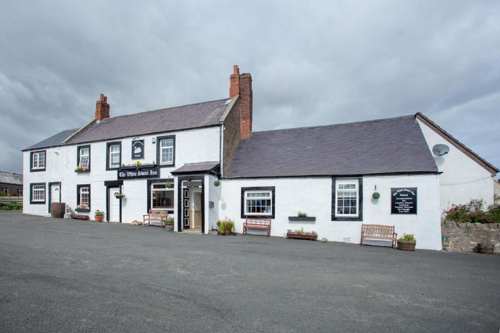 un bâtiment blanc avec bancs devant lui dans l'établissement The White Swan Inn, à Lowick