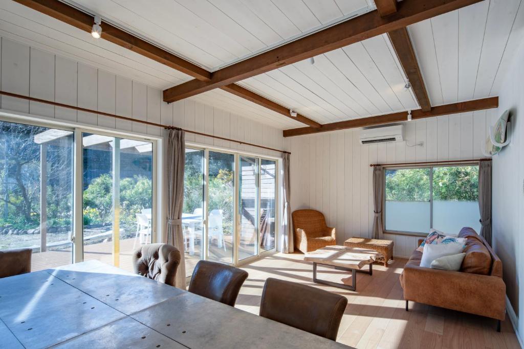 a living room with a table and chairs and windows at Sotoura Sunrise Cottage 30m from Beach in Shimoda