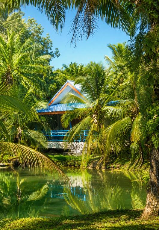 a house in the middle of a pond with palm trees at บ้านสวนลุงหวัด พังงา ใกล้ท่าเรือสุระกุล in Takua Thung