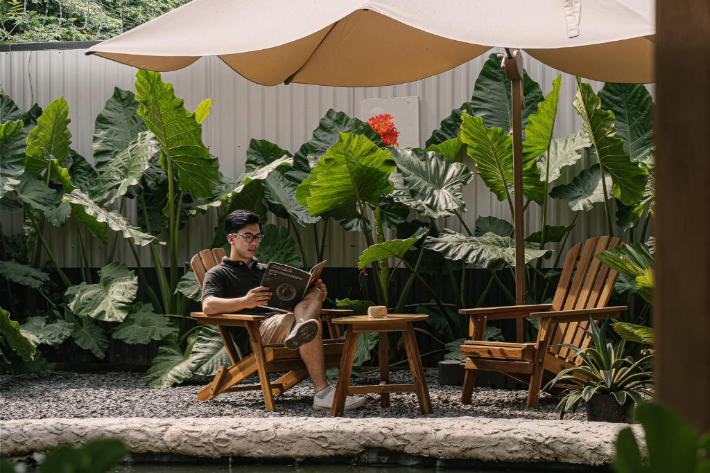 a man sitting in a chair under an umbrella at Modapick Bạch Đằng - Living in the nature garden with full river view in Hanoi