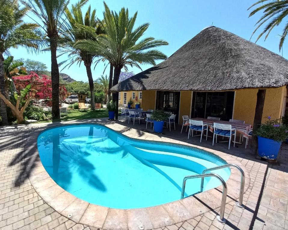 a resort with a large swimming pool with a thatch roof at Capbon Guesthouse in Windhoek
