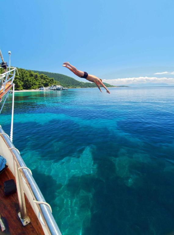 a person jumping into the water from a boat at Blue Green Bay in Panormos Skopelos