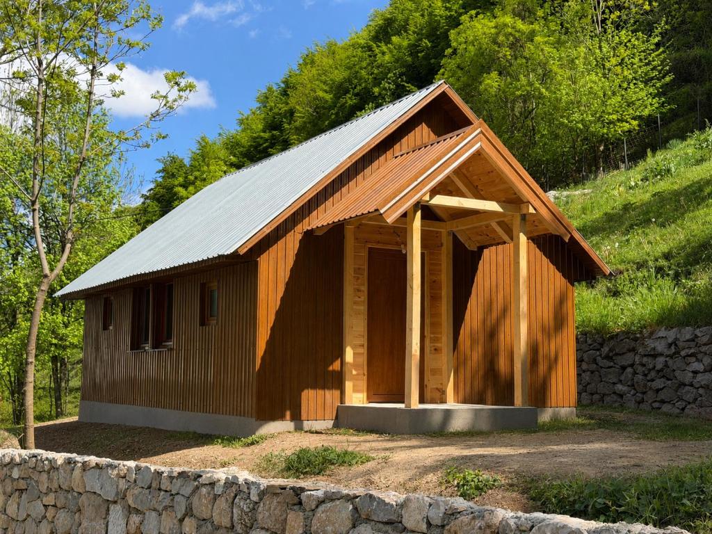 a wooden barn with a metal roof and a stone wall at Nature Guesthouse Vuthaj in Vusanje