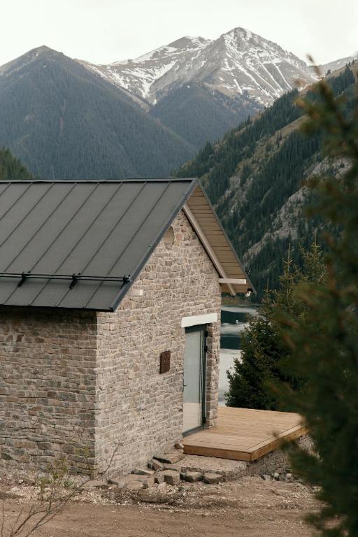 a stone building with a wooden deck in front of a mountain at Pana Unique Kolsay in Kurmenty