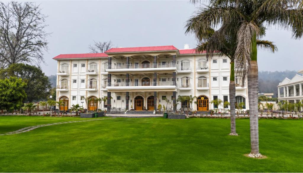 a large white building with a palm tree in the foreground at The Lychee Hotel & Resort by The Altruist in Rāmnagar