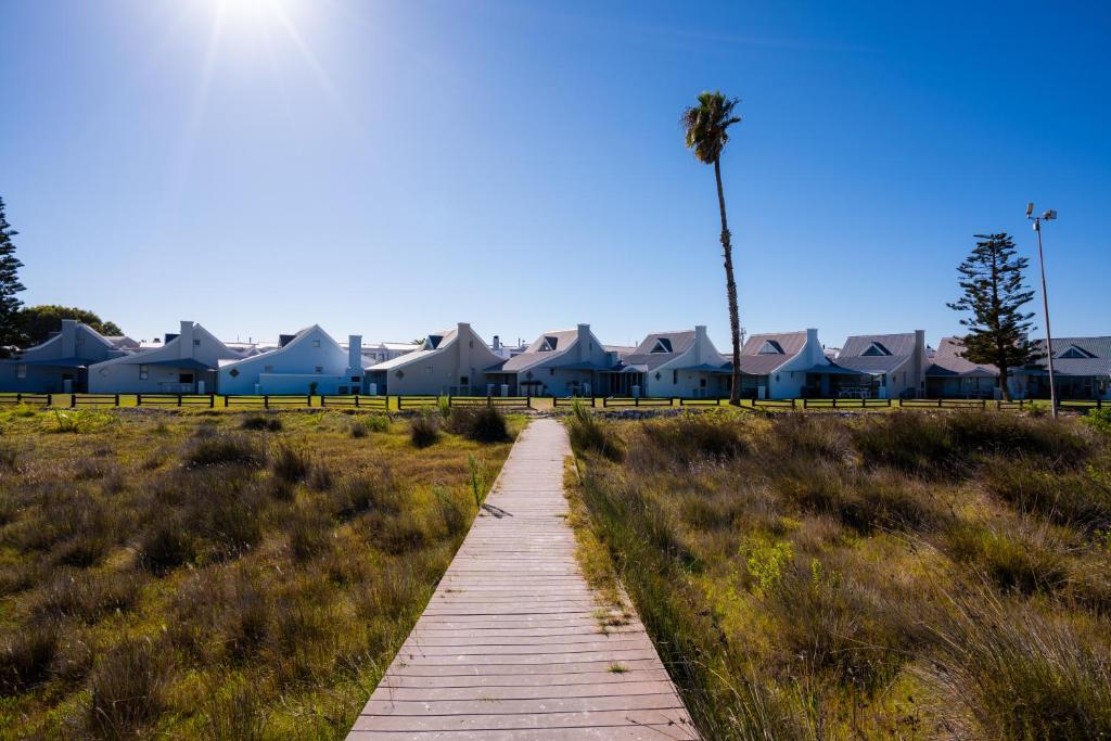 a wooden path leading to a beach with houses and a palm tree at Seabreeze Bungalow in Langebaan