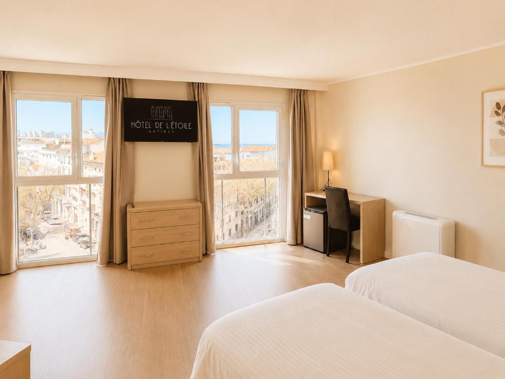 a hotel room with two beds and a desk and windows at Hôtel de l'Étoile in Antibes