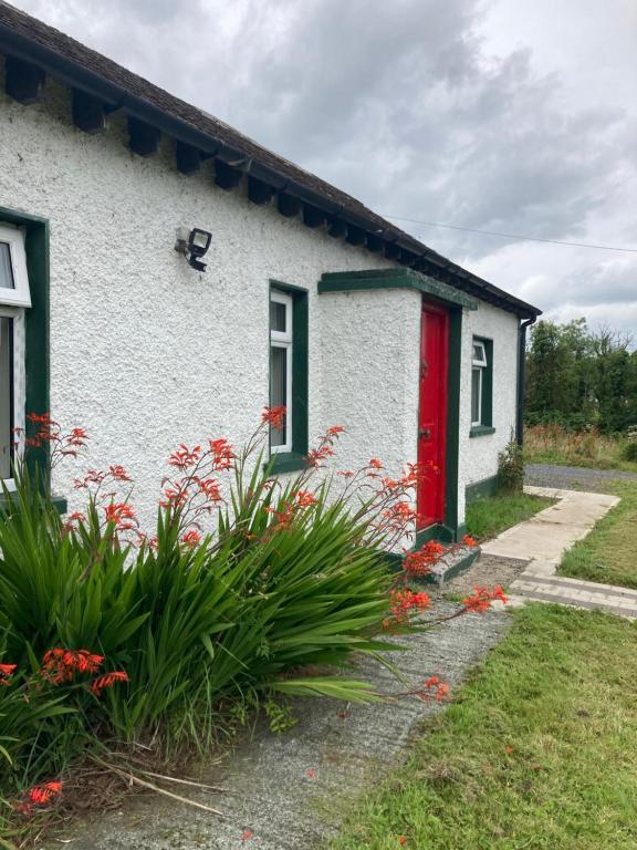 a white house with a red door and flowers at 3 bedroom Beautiful Cosy Cottage in Killashandra