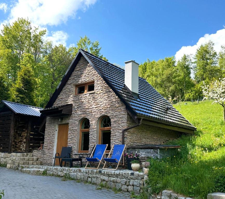a stone house with blue chairs in front of it at Agroturystyka Monte Luna domki in Czarnów