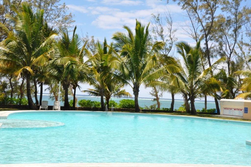 una piscina con palme e l'oceano sullo sfondo di Villas Right ON the Beach Belle Mare a Belle Mare