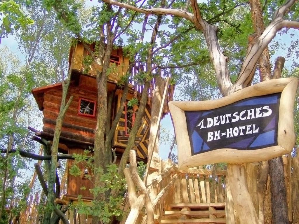 una casa en el árbol con un cartel delante en Baumhaushotel - Die geheime Welt von Turisede - Kulturinsel Einsiedel, en Zentendorf