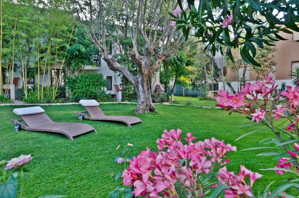 2 chaises et un arbre dans une cour ornée de fleurs roses dans l'établissement Hotel Santa Maria, à Santa Maria Navarrese