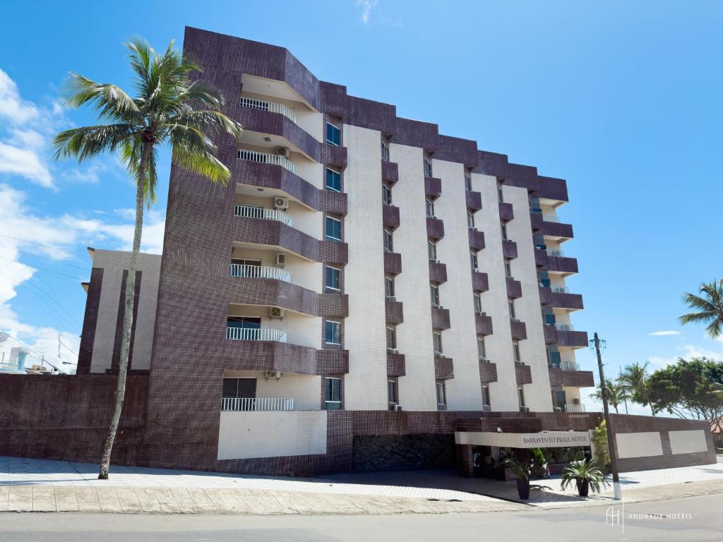 a tall building with a palm tree in front of it at Rede Andrade Barravento in Ilhéus