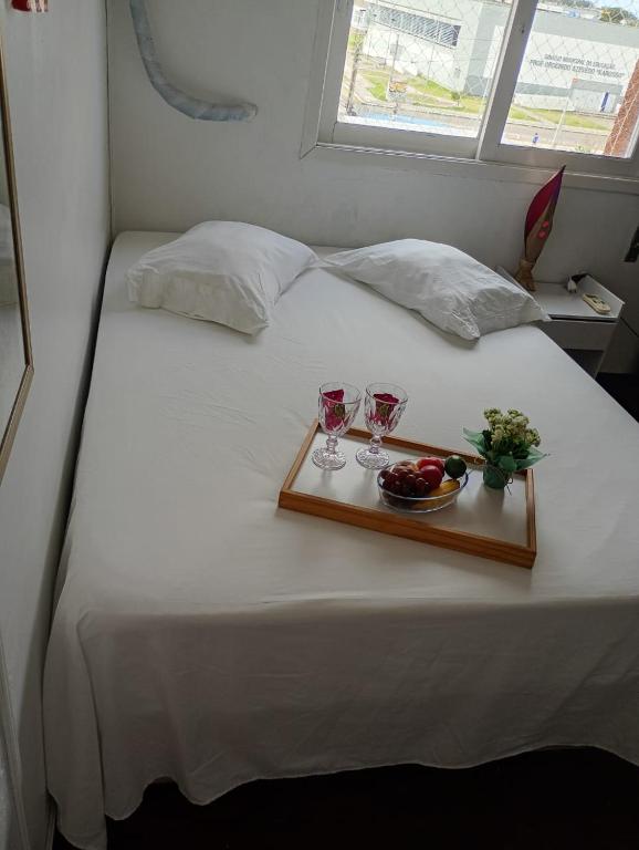 a tray with two glasses and a bowl of fruit on a bed at Conforto no Centro in Pelotas