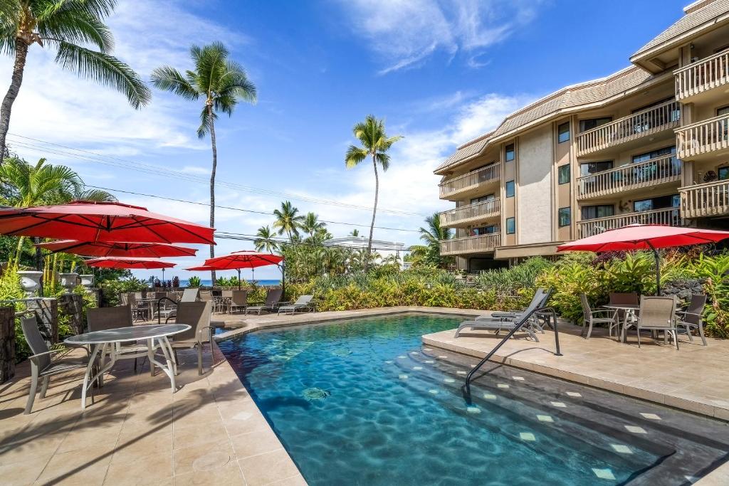 a pool at a resort with tables and chairs and umbrellas at KONA - Royal Kahili B205 End Unit - Gorgeous Views in Kailua-Kona