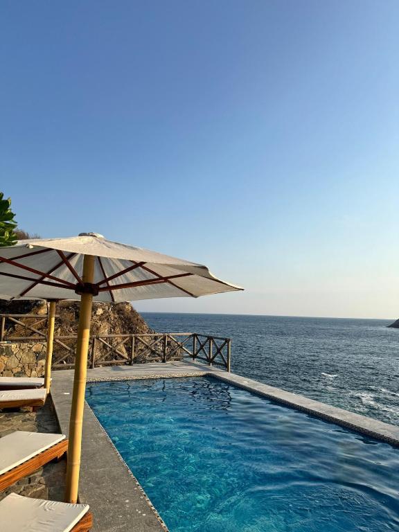 a swimming pool with an umbrella and the ocean at Casa Mario Alberto - Oceanfront Bungalows in Puerto Ángel