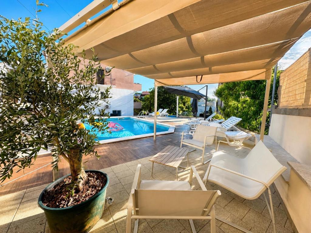 a patio with a tree and chairs and a pool at Oleander in Malinska