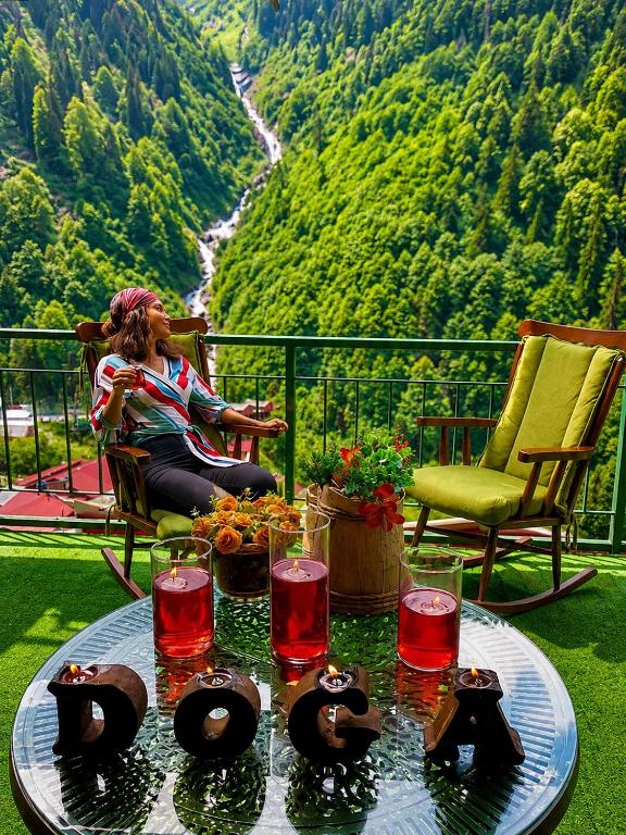 a woman sitting on a balcony with a table with wine glasses at Ayder Doga Resort in Ayder Yaylasi