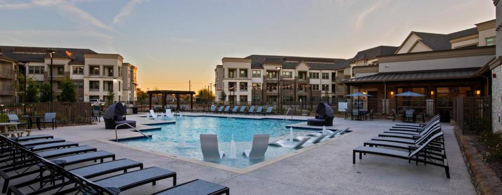 a swimming pool with chairs and tables and buildings at Luxury McKinney Resort Stay Near Universal Kids with Pool & Gym in McKinney
