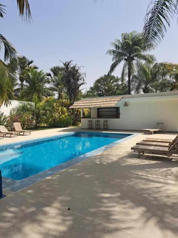 a swimming pool next to a house with palm trees at Cap DIOLA in Cap Skirring