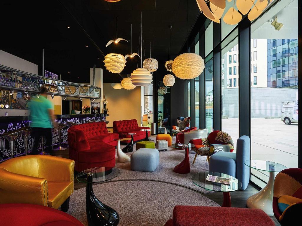 a lobby with red chairs and tables and windows at ibis Styles Liege Guillemins in Liège