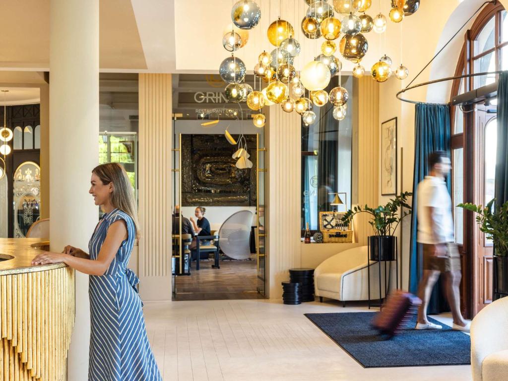 a woman standing at a counter in a lobby at Rezydent Hotel Sopot - MGallery Collection in Sopot
