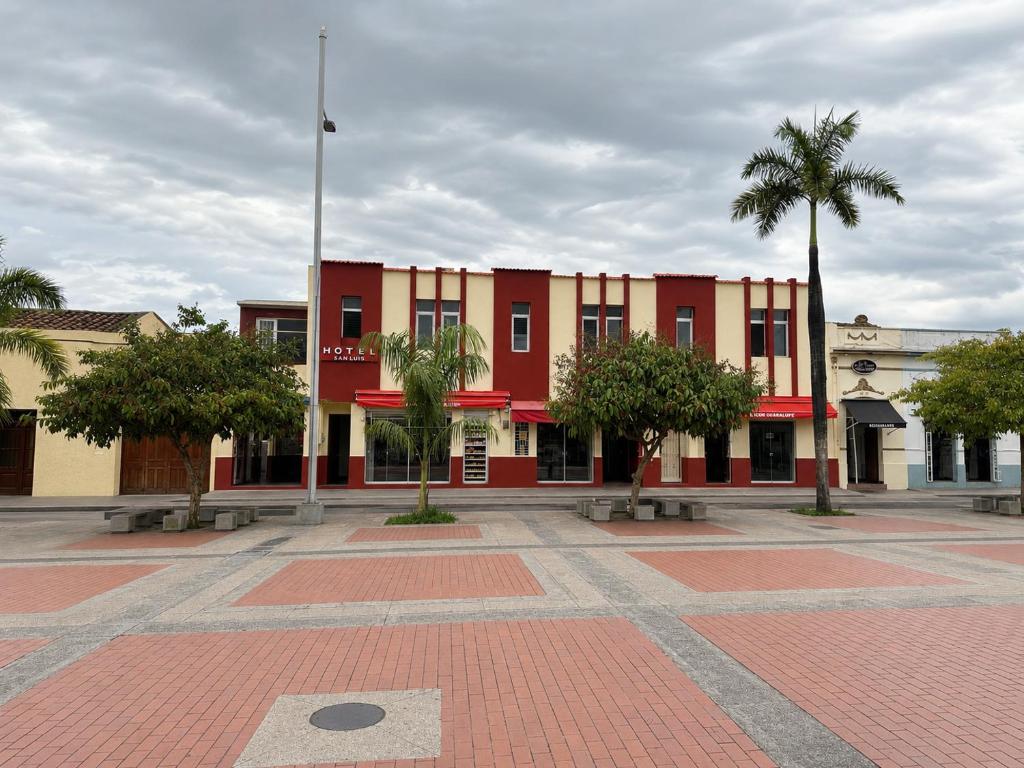 a red building with palm trees in a courtyard at Hotel San Luis in Buga