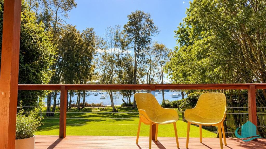 two chairs sitting on a porch with a view of the water at Wemberley Lakehouse in Wangi Wangi