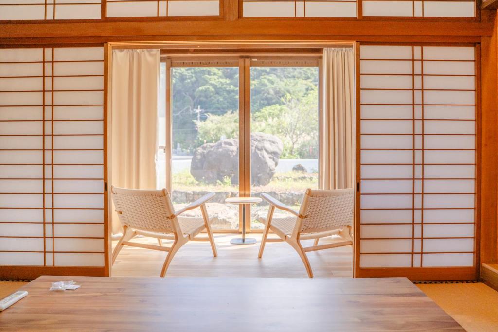 a room with two chairs and a table and a window at Umibe no yado yo-riyo-ri in Amami