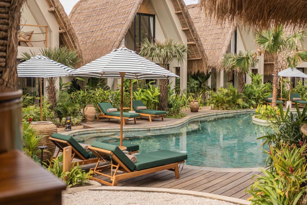a resort pool with lounge chairs and umbrellas at Hotel Together Bali in Uluwatu