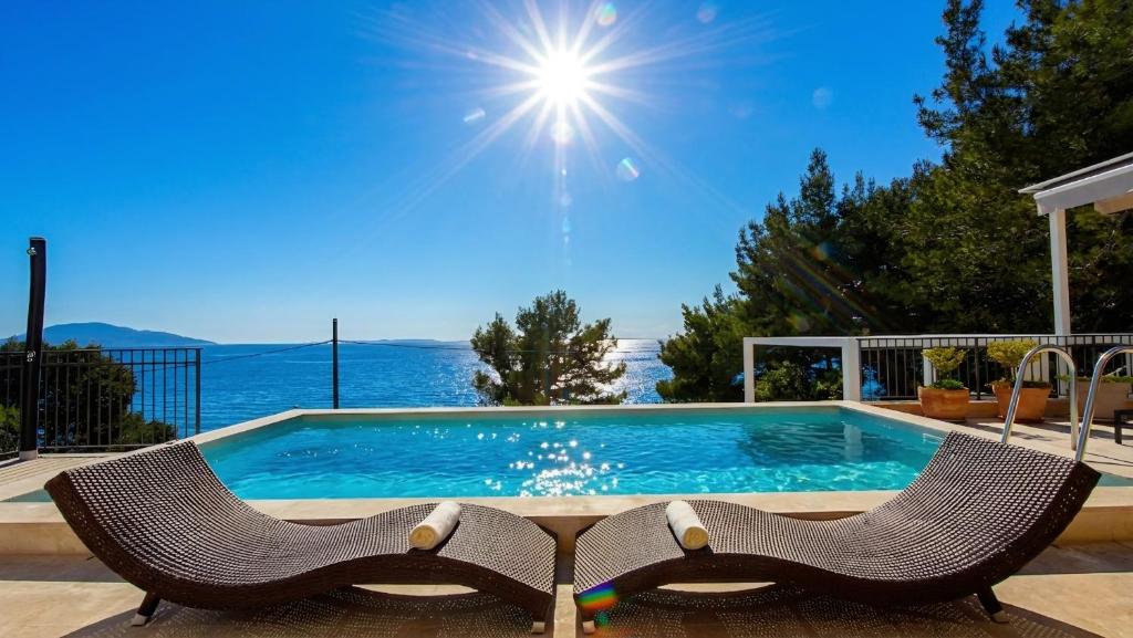 a swimming pool with two chairs and the ocean in the background at Villa St Martin-Reef - Exclusive Seafront Villa with Private Heated Pool in Martinšćica