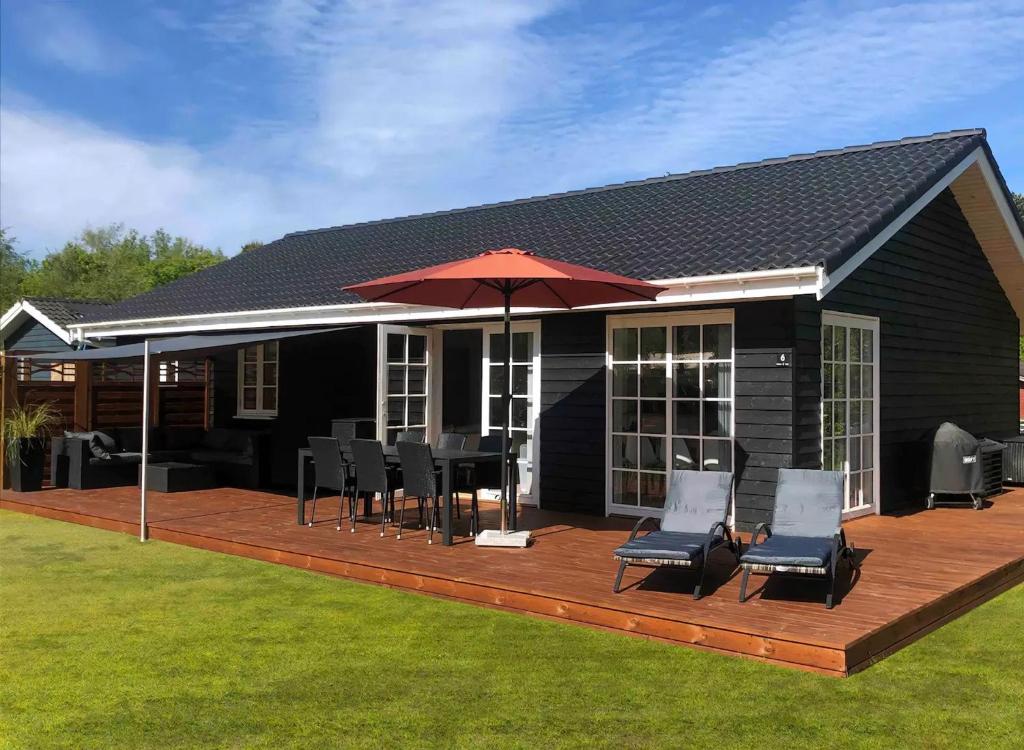a house with a deck with chairs and an umbrella at New Modern Holiday Home Near The Beach And City in Nykøbing Sjælland