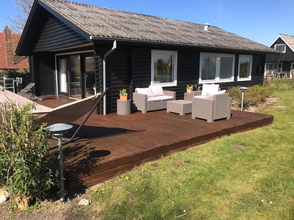eine Holzterrasse mit weißen Stühlen und einem Haus in der Unterkunft Ruhig Gelegenes Ferienhaus In Meeresnähe in Brenderup
