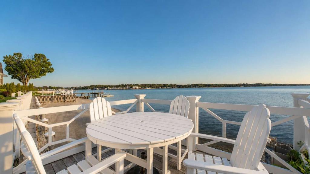 a white table and chairs on a deck with the water at Hampton Bays Townhouse - Pool Beach Access in Hampton Bays