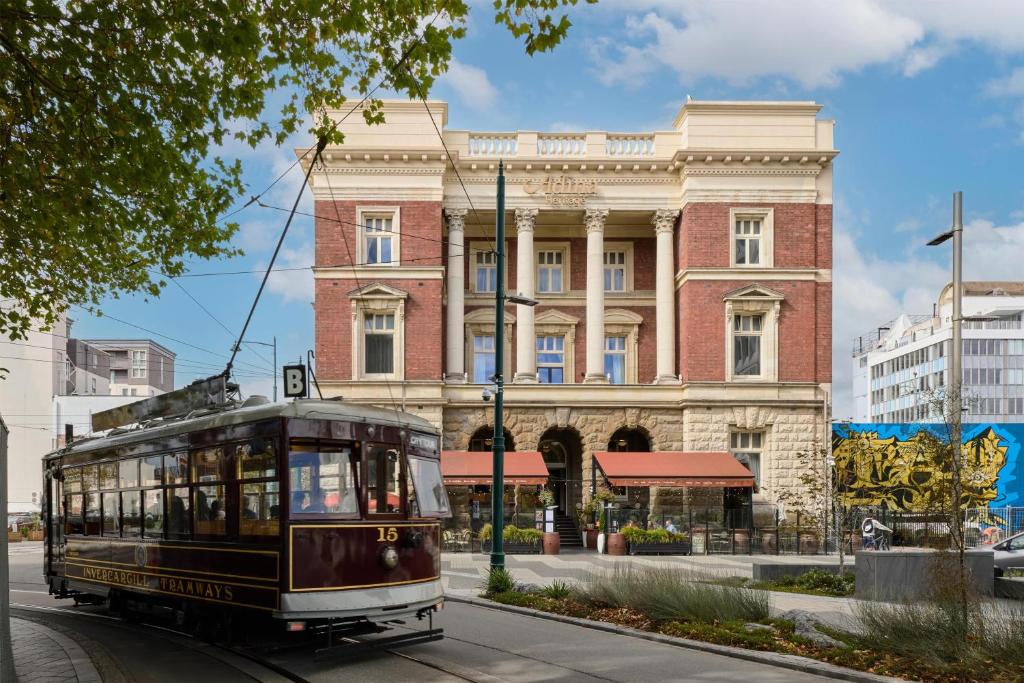 a trolley car driving down a street in front of a building at Adina Heritage Christchurch in Christchurch