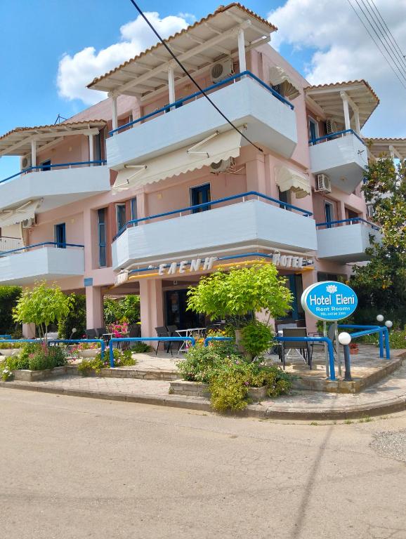 a large pink building with a blue sign in front of it at Hotel Eleni in Paralia Dionysiou