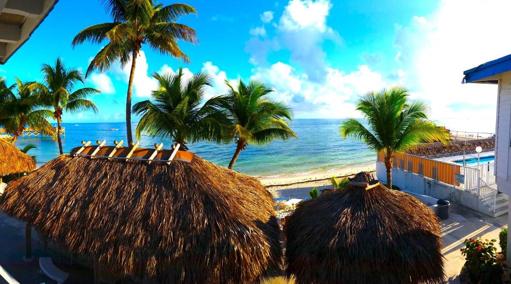 una playa con palmeras, cabañas de paja y el océano en Key Colony Beach Motel, en Marathon