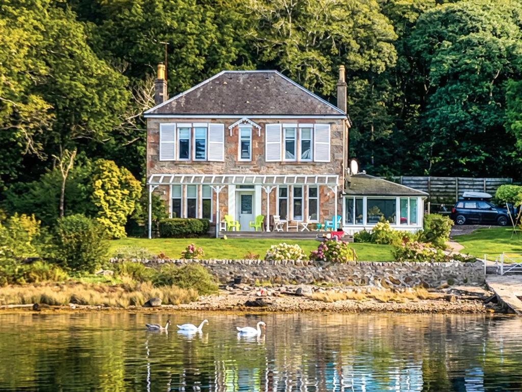 a house on the water with swans in front of it at Failte in Colintraive