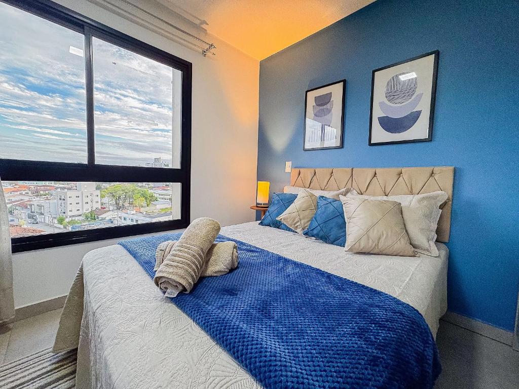 a bedroom with a bed with blue walls and a window at Apto no coração de Brusque in Brusque