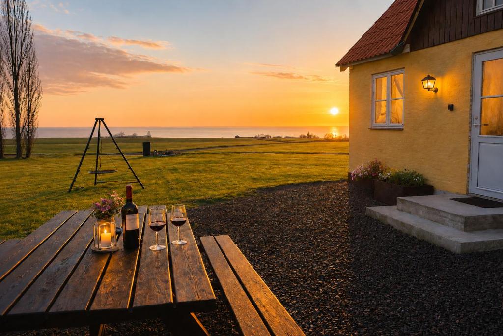 a wooden picnic table with a bottle of wine and a sunset at Solhjem Bornholm - Top Rated Sea View Stay in Gudhjem