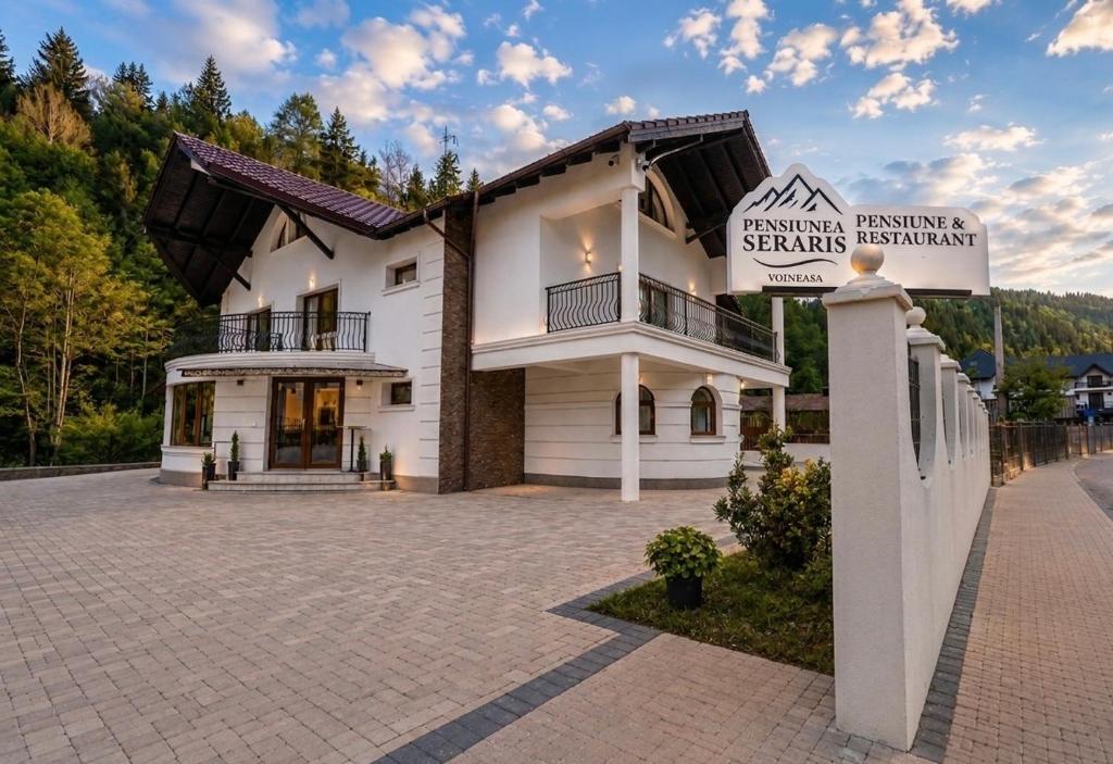 a large white building with a sign in front of it at Pensiunea Seraris in Voineasa