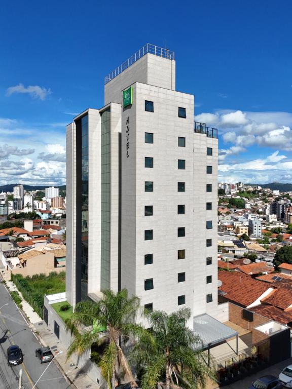 a tall white building with palm trees in front of a city at Íbis Styles Itaúna in Itaúna