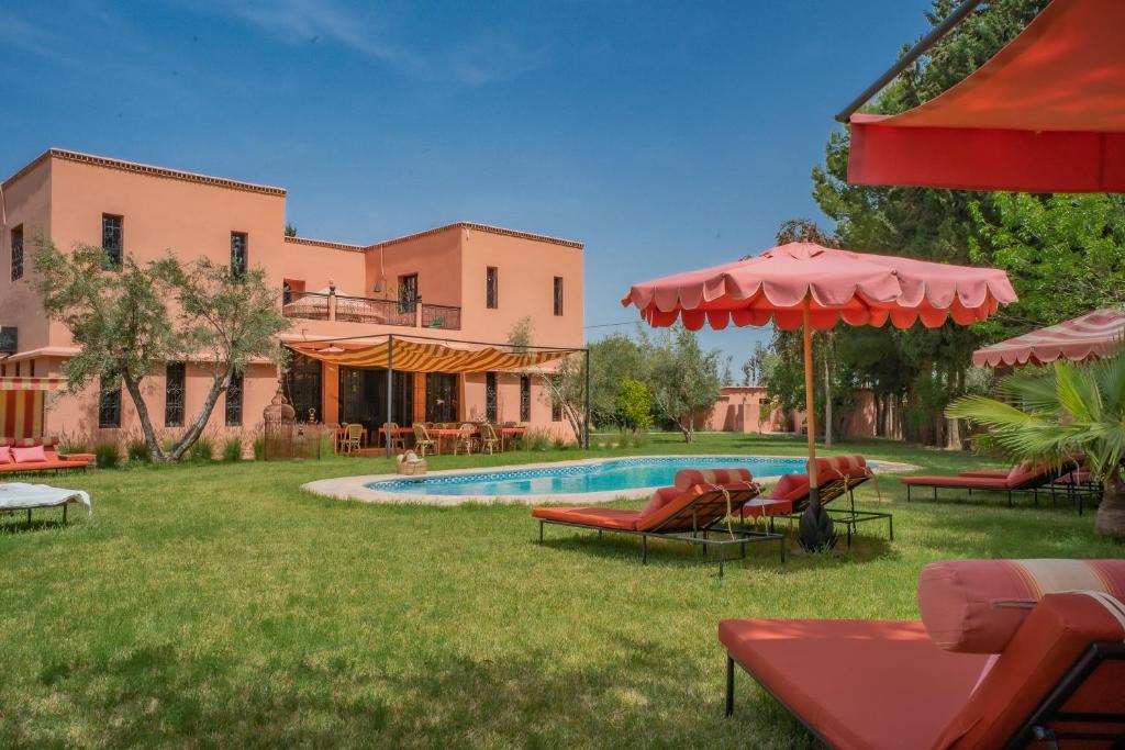 a pool with chairs and umbrellas in front of a house at Villa Samadhi - Luxury & Serenity in Marrakesh