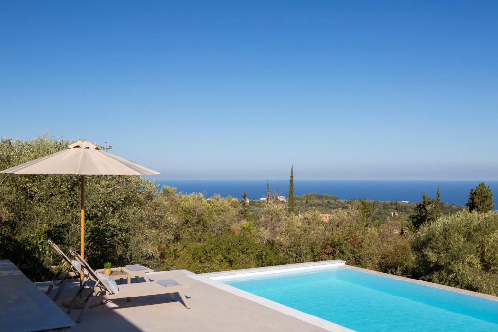 a swimming pool with an umbrella and chairs and the ocean at Ionian Harmony Luxury Villas in Tsoukalades