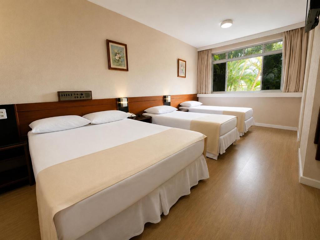 a hotel room with three beds and a window at Lira Hotel in Curitiba