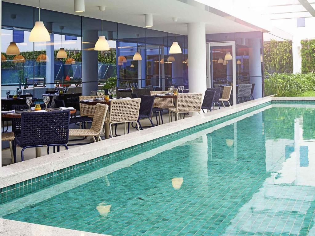 a swimming pool with tables and chairs next to a restaurant at Novotel Rio de Janeiro Parque Olimpico in Rio de Janeiro
