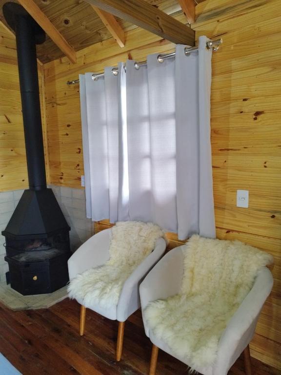 a living room with two white chairs and a stove at Cabana Família Lima in Urubici