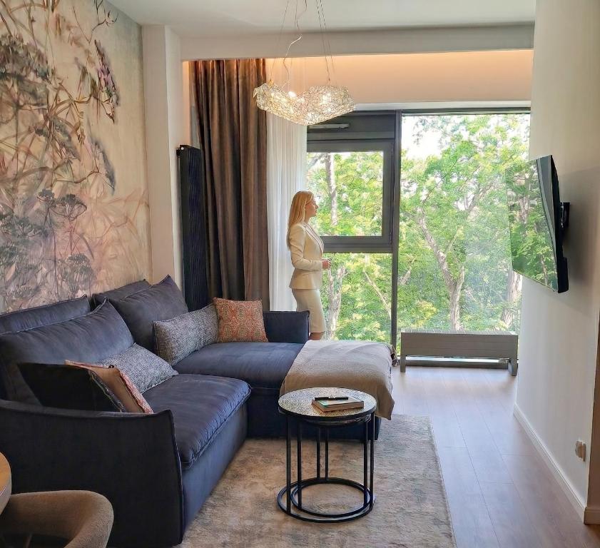 a woman standing in a living room looking out the window at Park View Olszynki Park in Rzeszów